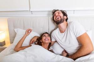 jeune couple d'amoureux dans le lit. jeune couple allongé dans son lit et riant tout en se chatouillant. heureux jeune couple sensuel allongé dans son lit ensemble le matin photo