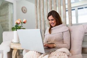 belle femme pigiste notant des informations pour la planification d'un projet faisant un travail à distance via un ordinateur portable. fille riant en lisant des e-mails sur un ordinateur portable moderne. photo