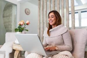 belle femme pigiste notant des informations pour la planification d'un projet faisant un travail à distance via un ordinateur portable. fille riant en lisant des e-mails sur un ordinateur portable moderne. photo