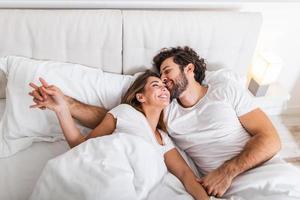 un couple heureux est allongé dans son lit ensemble. appréciant la compagnie les uns des autres.heureux jeune couple étreignant et souriant allongé sur le lit dans une chambre à la maison. photo