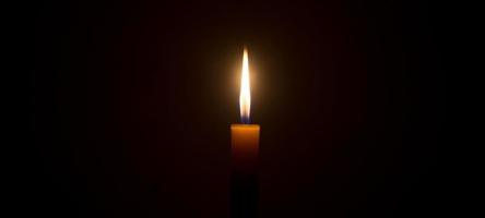 une seule flamme de bougie allumée ou une lumière rougeoyante sur une bougie blanche sur fond noir ou sombre sur une table à l'église pour noël, des funérailles ou un service commémoratif photo