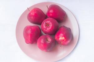 Pommes rouges fraîches en plaque rose isolé sur fond blanc photo