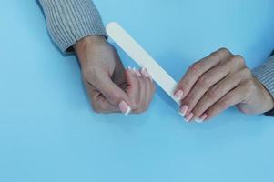 les mains féminines tiennent une lime à ongles blanche et corrigent la manucure. photo