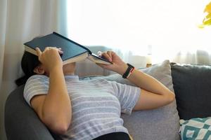 femme asiatique allongée sur le canapé du salon, elle a couvert son visage avec un livre pour faire une sieste pendant son temps libre. mise au point douce et sélective. photo