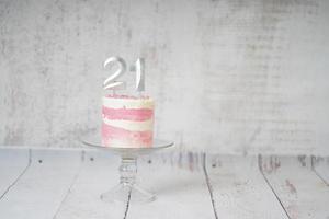 21ème gâteau d'anniversaire gâteau rose et argenté avec quelques pépites et 21ème chandelle sur un fond en bois blanc. photo