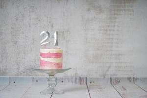 21ème gâteau d'anniversaire gâteau rose et argenté avec quelques pépites et 21ème chandelle sur un fond en bois blanc. photo