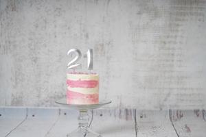 21ème gâteau d'anniversaire gâteau rose et argenté avec quelques pépites et 21ème chandelle sur un fond en bois blanc. photo