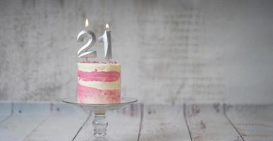 21ème gâteau d'anniversaire gâteau rose et argenté avec quelques pépites et 21ème chandelle sur un fond en bois blanc. photo