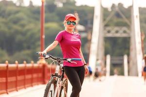 jeune fille blonde sexy aux cheveux longs en lunettes de soleil debout près du vélo, amusez-vous et bonne humeur en regardant à huis clos et souriant photo