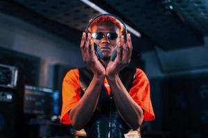 jeune artiste afro-américain debout dans un studio d'enregistrement et tenant des écouteurs