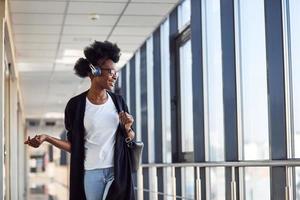 une jeune passagère afro-américaine en vêtements décontractés est à l'aéroport en écoutant de la musique dans des écouteurs photo