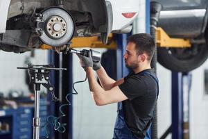 à l'aide d'un outil spécial. un homme en uniforme de travail répare une automobile blanche à l'intérieur. conception de service de voiture photo