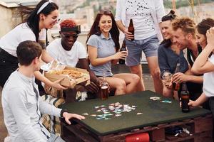 avec de délicieuses pizzas. un groupe de jeunes en vêtements décontractés fait la fête ensemble sur le toit pendant la journée photo