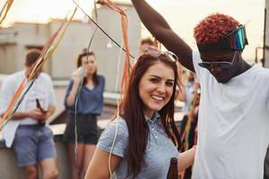 posant pour un appareil photo. un groupe de jeunes en vêtements décontractés fait la fête ensemble sur le toit pendant la journée photo