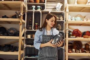 jeune femme céramiste à l'intérieur tenant un produit en argile fait main. conception de la poterie photo