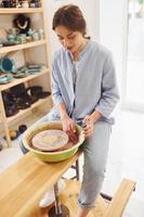 jeune femme céramiste travaillant en utilisant un tour de potier à l'intérieur et en fabriquant un produit en argile fait main photo