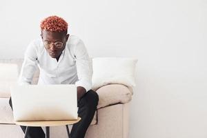 jeune homme afro-américain en vêtements formels assis à l'intérieur avec un ordinateur portable dans les mains photo