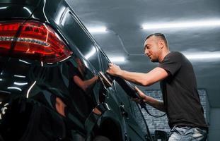 gars polissant la surface du véhicule. l'automobile noire moderne est nettoyée par l'homme à l'intérieur de la station de lavage de voiture photo