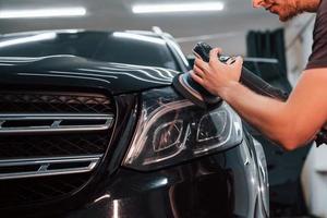 gars polissant la surface du véhicule. l'automobile noire moderne est nettoyée par l'homme à l'intérieur de la station de lavage de voiture photo