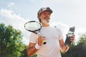 Senior homme élégant moderne avec une raquette à l'extérieur sur un court de tennis pendant la journée photo