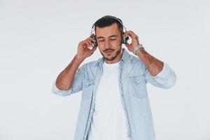 écoute la musique dans les écouteurs. jeune bel homme debout à l'intérieur sur fond blanc photo