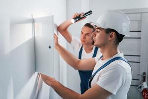 deux jeunes électriciens masculins travaillent ensemble à l'intérieur. à l'aide d'une lampe de poche photo