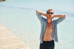 en lunettes de soleil. jeune homme européen passe des vacances et profite de temps libre sur la plage de la mer photo