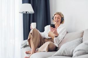 femme d'âge moyen dans des vêtements élégants est à la maison utilise le téléphone photo