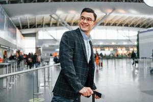 avec bagages. jeune homme d'affaires en vêtements formels est à l'aéroport pendant la journée photo