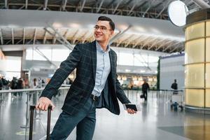 avec bagages. jeune homme d'affaires en vêtements formels est à l'aéroport pendant la journée photo