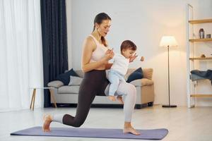 debout sur le tapis et faire des exercices. mère avec sa petite fille est à la maison ensemble photo