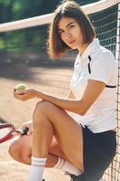 assis et tenant une raquette. La joueuse de tennis est sur le terrain pendant la journée photo