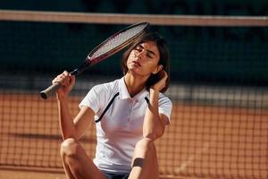 brune est assise sur le sol. La joueuse de tennis est sur le terrain pendant la journée photo