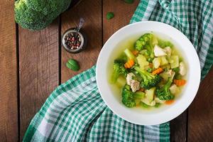 soupe au poulet avec brocoli, pois verts, carottes et céleri dans un bol blanc sur fond bois de style rustique. vue de dessus photo