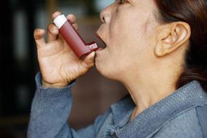 une patiente âgée utilise un inhalateur d'asthme brun pour soulager l'asthme. concept, soins de santé à domicile. produits pharmaceutiques pour le traitement des symptômes de l'asthme ou de la MPOC. utiliser sous ordonnance. photo