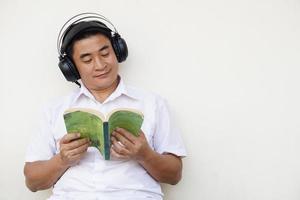 un homme asiatique lit un livre et porte un casque écoute de la musique douce pour se concentrer sur la lecture. concept, temps libre, passe-temps, passe-temps, se détendre avec de la musique. photo