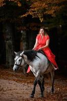 monter à cheval, marcher dans une forêt d'automne, une femme à cheval dans une longue robe rouge pieds nus. photo