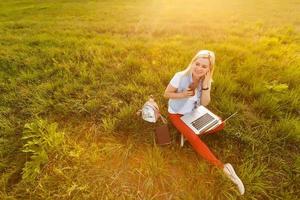 jeune femme avec ordinateur portable assis sur l'herbe verte photo
