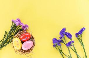 oeufs de pâques dans la décoration de nid de panier avec marguerite de fleur pourpre et fleurs de statice sur fond jaune photo