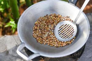 grains de café torréfiés sur une poêle chaude dans la campagne de montagne - grains de café crus frais photo