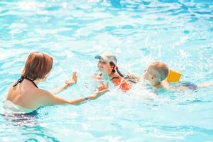 belle jeune mère avec petit fils et fille dans la piscine. photo