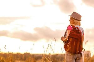 hipster jeune fille avec sac à dos en profitant du coucher du soleil. voyageur touristique sur fond. photo