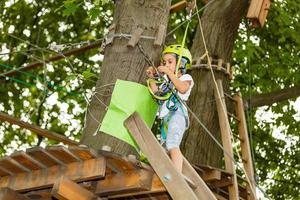 adorable petite fille profitant de son temps dans le parc d'aventure d'escalade lors d'une journée d'été chaude et ensoleillée. activités d'été pour les jeunes enfants. enfant s'amusant pendant les vacances scolaires. photo