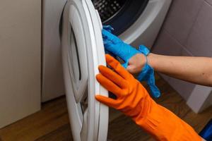 main dans un gant déchiré nettoyant la machine à laver. nettoyage régulier. la femme de chambre nettoie la maison.