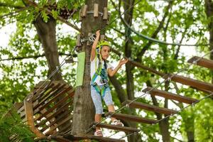 petite fille est debout sur une corde, tenant une corde avec ses mains. un enfant dans un parc à cordes passe des obstacles photo