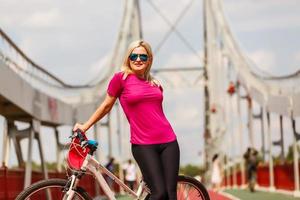 jeune fille blonde sexy aux cheveux longs en lunettes de soleil debout près du vélo, amusez-vous et bonne humeur en regardant à huis clos et souriant photo