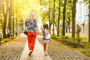 parent et élève de l'école primaire vont de pair. femme et fille avec sac à dos derrière le dos. début des cours. premier jour d'automne photo