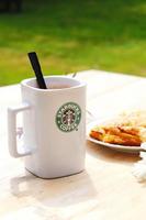 washington, états-unis - 01 août 2022 tasse à café avec logo starbucks sur le devant, boulangerie blanche sur assiette. placez-le sur une table en bois dans le jardin où le soleil du matin brille. photo