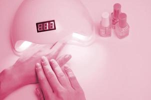 mains d'une jeune femme à la procédure de manucure en gros plan sur une image d'arrière-plan rose pastel aux tons de viva magenta, couleur de l'année 2023 photo