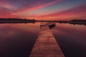 jetée en bois colorée sur un lac totalement calme au coucher du soleil photo